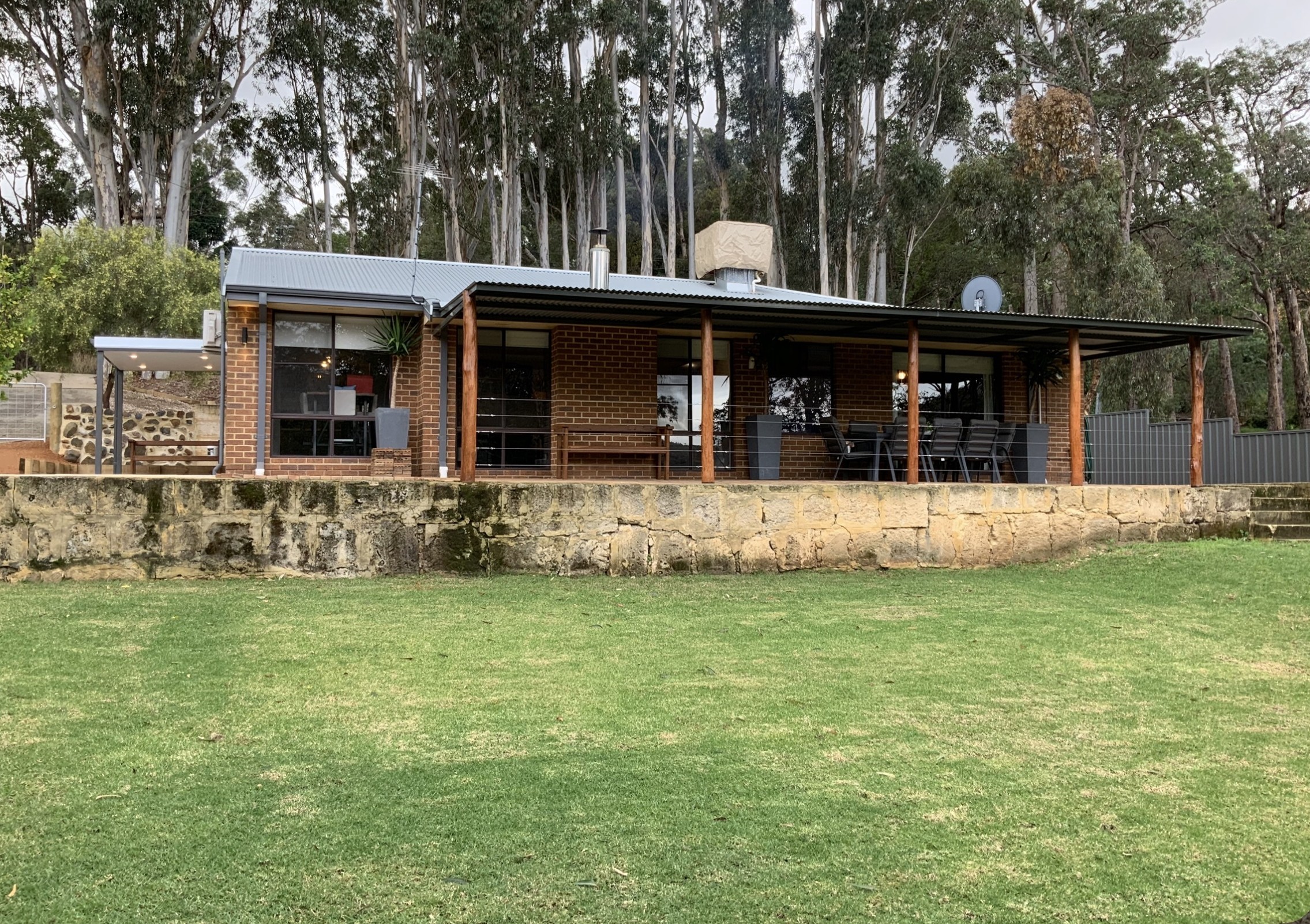  Brick lifestyle home with stone retaining wall, large lawn, towering eucalyptus backdrop